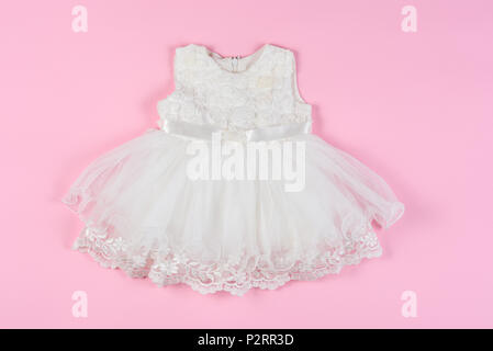 White baby dress with flowers on a pink background. Concept of children's clothing, fashionable children's clothes. Stock Photo