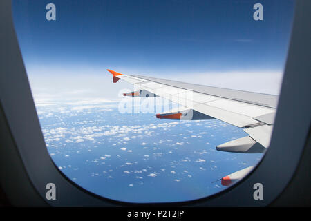 Looking through aircraft window during flight. Aircraft wing over blue skies and white clouds. Tasmania, Australia. Stock Photo