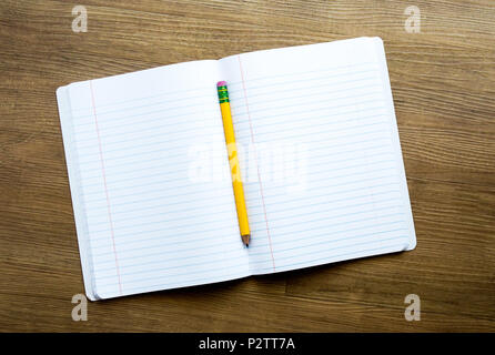 yellow pencil on top of a notebook with blank pages for customized message on a wooden desk Stock Photo