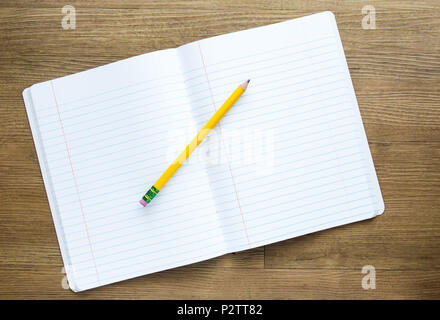 yellow pencil on top of a notebook with blank pages for customized message on a wooden desk Stock Photo