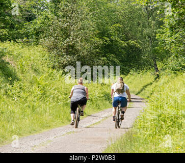 A overweight young couple cycling on a disused railway track, England, UK Stock Photo