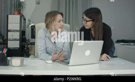 Two female colleagues discussing new project idea using laptop Stock Photo