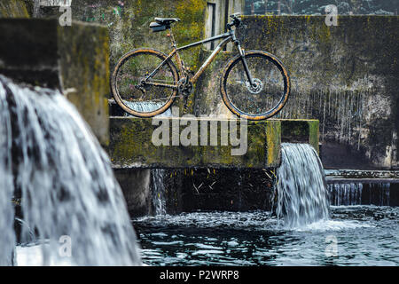 Dirty Mountain Bike Covered with Mud After Riding in Bad Weather Stands. Grey 29er Hardtail Bike on a Concrete Slab Against the Backdrop of an Urban W