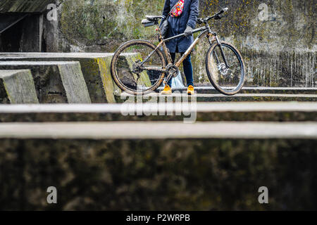 Figure of a Man Next to a Dirty Mountain Bike Against the Background of Old Urban Concrete Structures. Dirty Mountain Bike Covered with Mud After Ridi Stock Photo