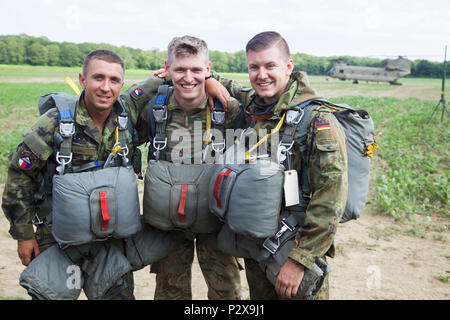 A Czec, British, and German Paratrooper has their photo taken with a CH-47 F Chinook Helicopter in the background during Leapfest 2016 at the University of Rhode Island, West Kingston, R.I., August 6, 2016. Leapfest is the largest, longest standing, international static line parachute training event and competition hosted by the 56th Troop Command, Rhode Island Army National Guard to promote high level technical training and esprit de corps within the International Airborne community. (U.S. Army photo by Sgt. Austin Berner/Released) Stock Photo