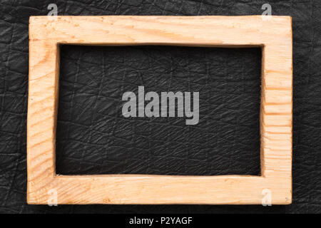 Beautiful wooden frame cut from a solid board, lies on a black leather. View from above Stock Photo