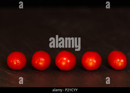Red baby plum tomatoes isolated on a dark background on a slate surface. Fruit healthy eating concept Stock Photo