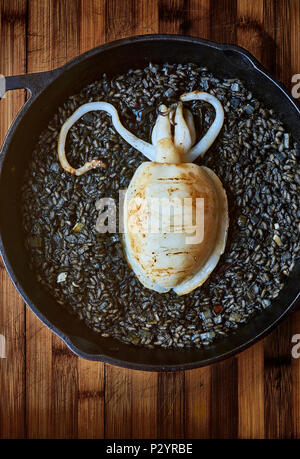 A pan of Black rice with cuttlefish on a rustic wooden board. Stock Photo