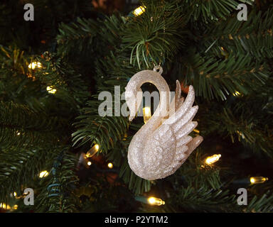 Closeup of a glittery white swan ornament hanging in a green Christmas tree with twinkling white LED string lights. Stock Photo