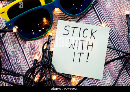 Stick with it motivational concept in business on notepaper. Two sunglasses of different colors with retro wooden background. LED lights are shown in  Stock Photo