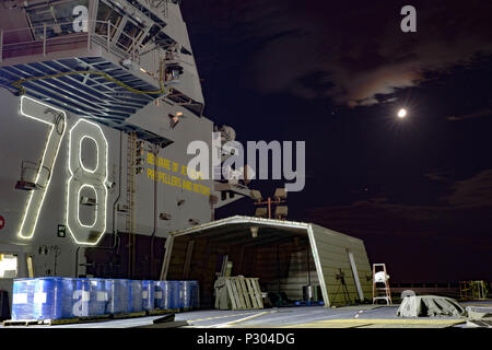 The Pre-Commissioning Unit Gerald R. Ford (CVN 78) aircraft carrier’s superstructure and flight deck are illuminated at night on August 11, 2016, while under construction at Huntington Ingalls Industries Newport News Shipbuilding. The first-in-class Ford-class carrier is designed to support modern naval aviation operations, featuring advanced catapult systems, nuclear propulsion, and an expanded flight deck for aircraft launch and recovery. Construction continues with naval personnel supervising progress and ensuring operational specifications. Stock Photo