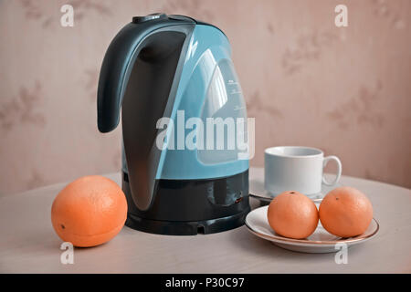 On the table is an electric kettle, next are oranges and tangerines. Stock Photo