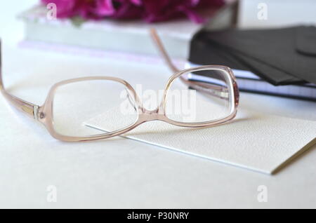 Bold violet pink peonies with blush pink glasses on a desk. Elegant feminine styled desktop workspace. Concept of working from home office, studying. Stock Photo