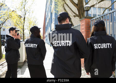 Rear View Of Security Guards In Black Uniform Standing Outside Building Stock Photo