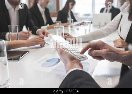 Group of business people in meeting room at office discuss financial reports, focus on male hands counting on calculator Stock Photo