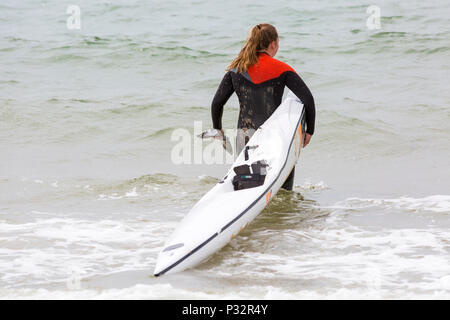 Branksome Chine, Poole, Dorset, UK. 17th June 2018. UK weather: breezy day at Branksome Chine beach, doesn't deter visitors going to the seaside. Young woman carrying surfski surf ski into the sea. Credit: Carolyn Jenkins/Alamy Live News Stock Photo