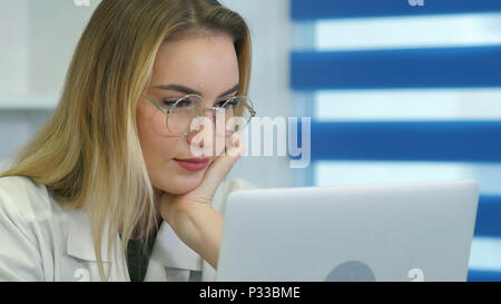 Young female nurse in glasses using laptop at desk in medical office Stock Photo