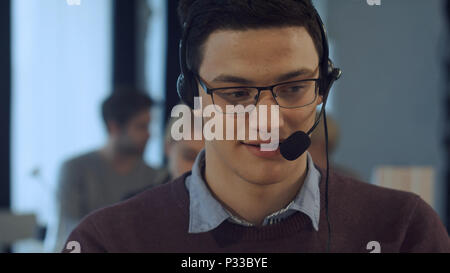 Young man working at a computer in a call centre smiling Stock Photo