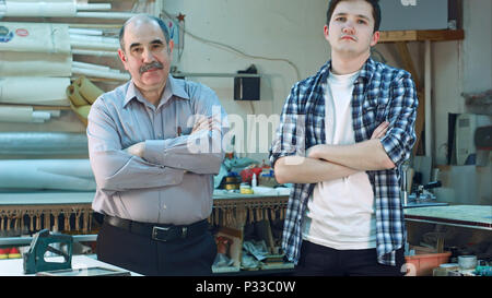 Portrait of two workers, standing in workshop and looking at camera seriously Stock Photo