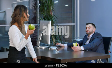 Two office workers having a break, aeting green apples and talking in office Stock Photo