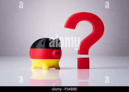 Close-up Of Piggybank Painted With German Flag And Red Question Mark Sign On Reflective Background Stock Photo