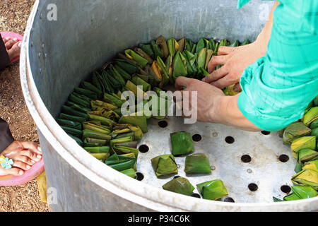 Packing banana leaf parcels of sweetmeats into a large pot ready for boiling over an open fire. Part of the preparation for the wedding day. Stock Photo
