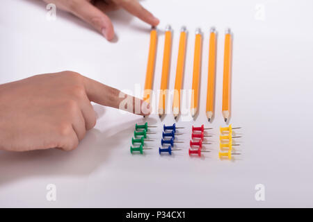 A Person's Hand Arranging Pencils And Multi Colored Pushpins In A Row On White Background Stock Photo