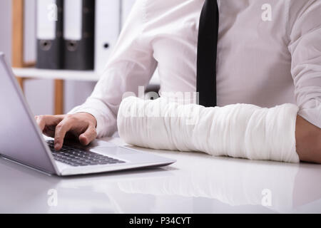 Close-up Of A Man With Fractured Hand Using Laptop Over Desk Stock Photo