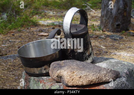 An old metal tea pot and cooking pan near a fireplace in the forest Stock Photo