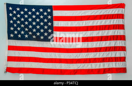 Worn american flag hanging from wall on a blank white wall Stock Photo