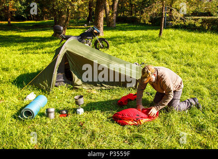 elderly tourist foldjng a tent in the forest on sunny summer day Stock Photo
