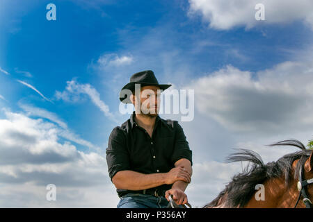 Good looking, hunky cowboy rides horse with boots, chequered shirt and hat Stock Photo