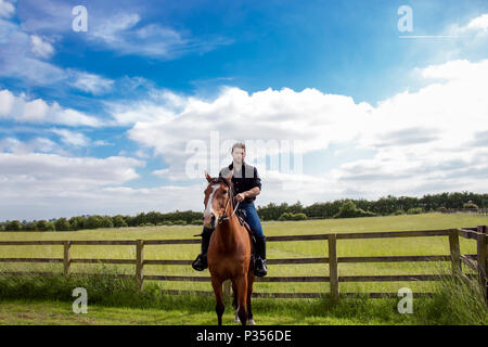 Good looking, hunky cowboy rides horse with boots, chequered shirt and hat Stock Photo