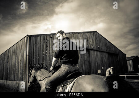 Good looking, hunky cowboy rides horse with boots, chequered shirt and hat Stock Photo