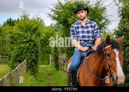 Good looking, hunky cowboy rides horse with boots, chequered shirt and hat Stock Photo