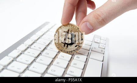hand holds a golden coin of bitcoin above the keyboard Stock Photo