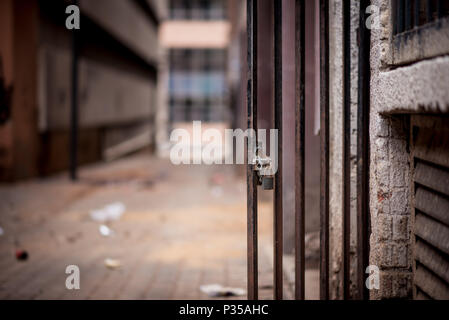 A metal barred doorway with a padlock standing open against the background of a dirty alley way in Johannesburg inner city Stock Photo