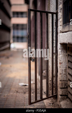 A metal doorway with padlock stands open in a dirty alleyway. Johannesburg inner city Stock Photo