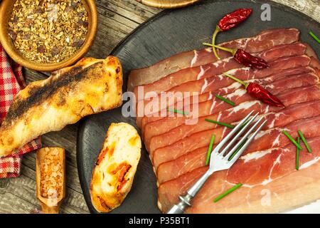 Thinly sliced German black forest ham with sliced ciabatta bread. Sliced and smoked ham with schwarzwald ham or prosciutto. Traditional German food Stock Photo