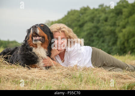 woman with bernese mountain dog lying on dry grass, looking at camera Stock Photo