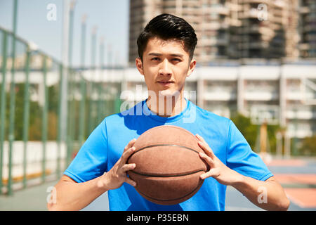 young asian male player holding a basketball looking at camera. Stock Photo