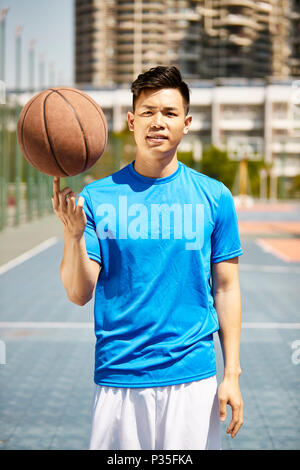 young asian man holding a basketball on finger looking at camera. Stock Photo