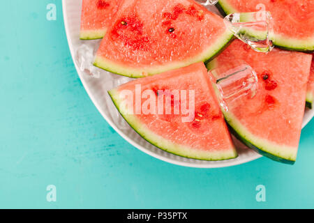 Closeup of fresh cut watermelon slices on ice cubes on plate on blue background. Summer concept Stock Photo