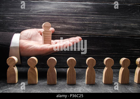 A businessman holds a wooden leader figure on the palm of his hand over a number of other workers. Concept leader, team work. Business and department  Stock Photo