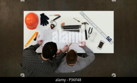Architect working on laptop while his colleague bringing more drawings Stock Photo