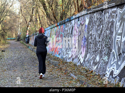 Berlin, Germany, woman jogging along a graffiti-strewn wall Stock Photo