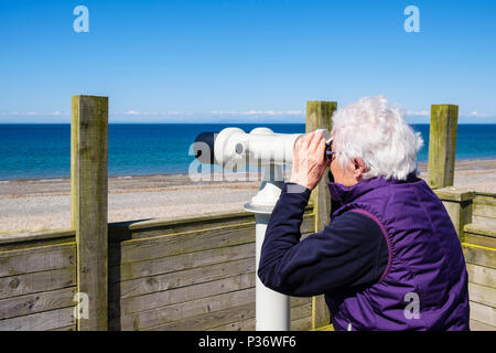 Senior elderly woman looking at sea birdwatching through a telescope at Ayres visitor centre. Point of Ayre, Ramsey, Isle of Man, British Isles Stock Photo