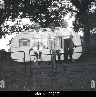 1951, historical, group of three young adult women -possibly sixth-formers or college students - on holiday, sitting on a fence infront of their caravan, England, UK. Stock Photo