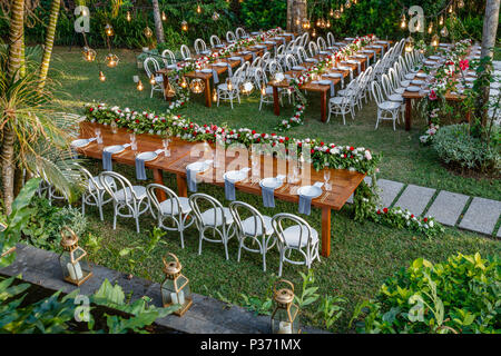 Set tables for a wedding dinner in a tropical garden decorated with rose and chrysanthemums garlands. Concept of a tropical wedding.  Bali, Indonesia. Stock Photo