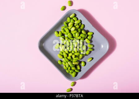 Green fresh soybeans on gray square plate on pink background. Healthy food concept flat lay with coppy space. Top view. Stock Photo